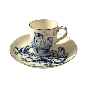 May include: A blue and white porcelain teacup and saucer set with a gold trim. The cup and saucer feature a whimsical illustration of children playing with a wheelbarrow.