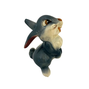 May include: A ceramic figurine of a gray rabbit with red ears and brown eyes. The rabbit is standing on its hind legs with its front paws raised.