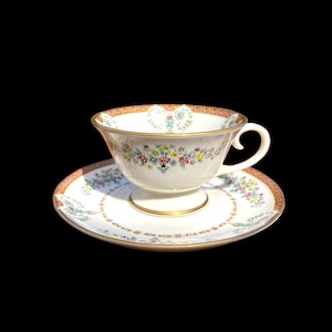 May include: A white teacup and saucer with a floral pattern in shades of red, yellow, and green. The cup has a gold rim and the saucer has a gold band around the edge.