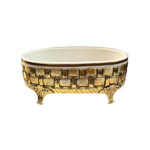 May include: Oval-shaped white ceramic dish with a gold-coloured woven design around the rim and three gold-coloured feet.