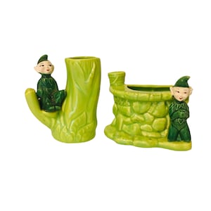 May include: Two green ceramic planter pots shaped like a tree stump and a stone cottage. Each pot features a small green elf figurine.