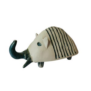 May include: A ceramic sculpture of a stylized animal with a long, curved trunk, striped body, and four legs. The sculpture is painted in shades of white and green.