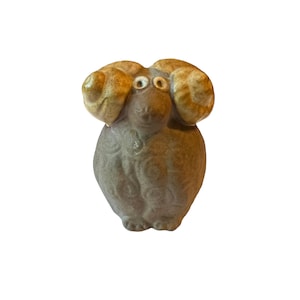 May include: A small ceramic figurine of a brown owl with large, yellow ears. The owl has large, black eyes and a textured body.