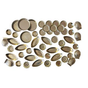 May include: An assortment of vintage brass decorative elements, including small round dishes, oval trays, and flower-shaped accents. The pieces have a tarnished, antique finish, and are arranged on a white background.