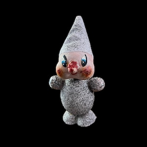 Könnte beinhalten: Ein vintage Weihnachtsornament in Form eines Schneemanns mit einer weißen und silbernen Glitzer-Oberfläche. Der Schneemann hat eine rote Nase, blaue Augen und einen weißen Hut.