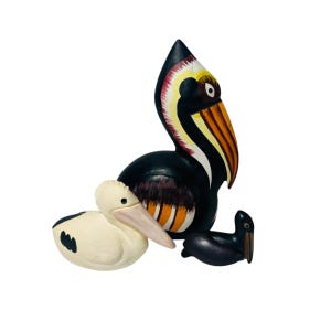 May include: Three wooden pelican figurines. The largest is black with a yellow, orange, and white beak. The middle-sized pelican is white with black markings. The smallest is black. All are hand-painted and have a glossy finish.