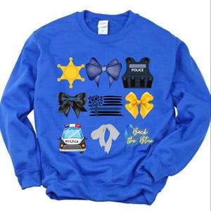 May include: Royal blue sweatshirt with a variety of blue and yellow graphics, including a police badge, a police car, a blue ribbon, and the text "Back the Blue".