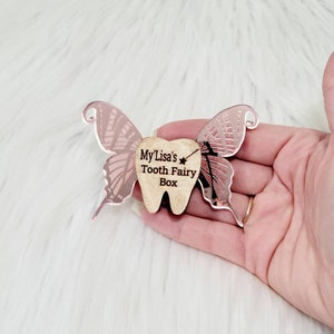 May include: A pink tooth fairy box with a butterfly design. The box is made of wood and has the text "My Lisa's Tooth Fairy Box" engraved on it.
