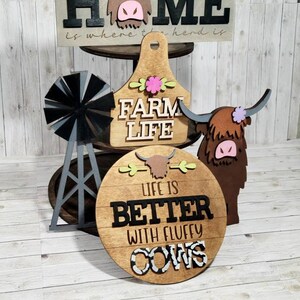 Op de afbeelding: Houten boerderijdecor met een hooglandkoe-thema. De borden lezen "Home is where the herd is", "Farm Life" en "Life is Better with Fluffy Cows".