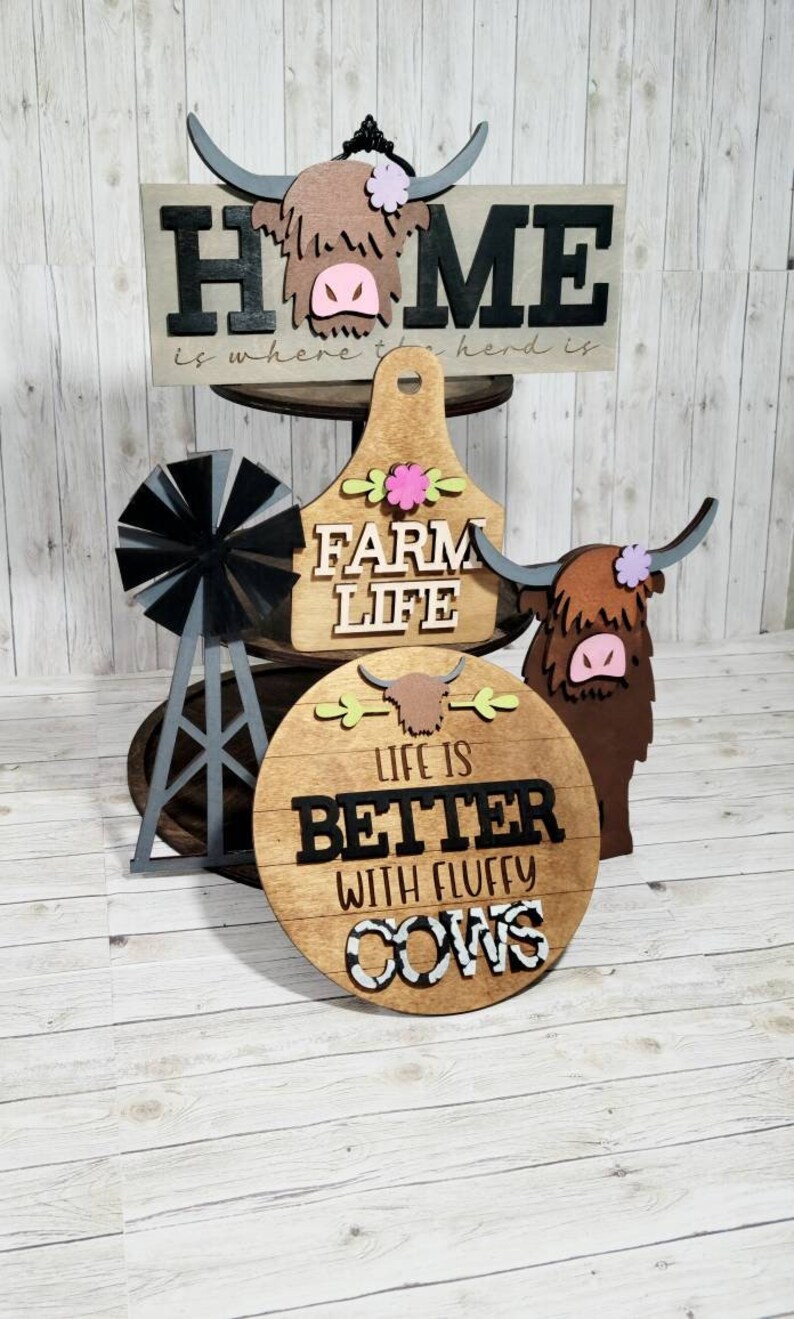 Op de afbeelding: Houten boerderijdecor met een hooglandkoe-thema. De borden lezen "Home is where the herd is", "Farm Life" en "Life is Better with Fluffy Cows".