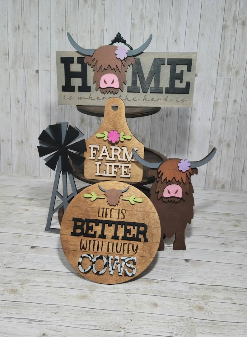 Op de afbeelding: Houten boerderijdecor met een hooglandkoe-thema. De borden lezen "Home is where the herd is", "Farm Life" en "Life is better with fluffy cows".