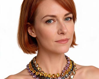 May include: A layered necklace with large, colourful gemstones in shades of purple, yellow, black, and clear. The necklace is worn around the neck, displaying the variety of colours and shapes of the stones. A statement piece of jewellery.