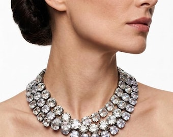 May include: A multi-strand statement necklace featuring three rows of clear, faceted, square-cut crystals set in a silver-toned metal frame. The crystals are arranged in a dense, uniform pattern that encircles the neck, creating a brilliant, reflective appearance.