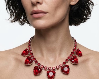 May include: A silver-toned necklace featuring a series of small, round, faceted red crystals along the chain, accented by five larger, prominent, heart-shaped red crystals suspended at intervals, creating a bold and vibrant statement piece.