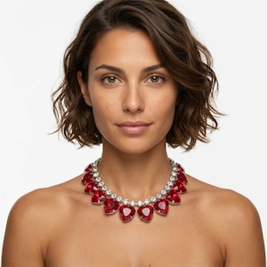 May include: A statement necklace featuring a row of large, faceted, triangular red crystals alternating with smaller, round, clear white crystals set in a metallic frame that rests against the base of the neck in a collar style arrangement.