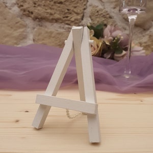 Può includere: Cavallo da cavalletto in legno bianco con una catena di perle attaccata alla parte inferiore. Il cavalletto è su una superficie in legno chiaro.