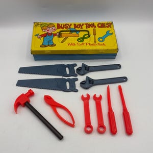 May include: A vintage toy tool set featuring a yellow and blue metal toolbox with the words "Busy Boy Tool Chest". The set includes plastic tools like saws, wrenches, a hammer, pliers, and screwdrivers. The toolbox has a cartoon illustration.