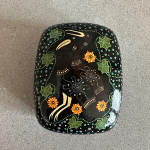 May include: Black rectangular box with a decorative floral design. The box features orange flowers, green leaves, and white and blue accents. The design is set against a black background.