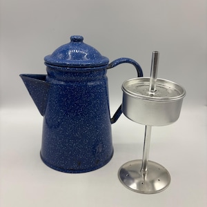 May include: A blue speckled enamelware coffee pot with a lid and handle, next to a stainless steel coffee filter assembly. The coffee pot has a spout for pouring. The filter assembly includes a perforated basket and a stand.