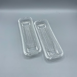 May include: Two clear glass serving dishes with a textured design. The dishes are rectangular and have a slightly curved edge.