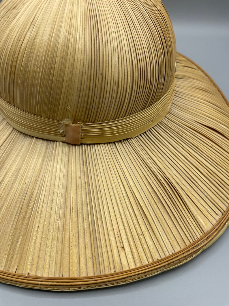 Puede incluir: Un sombrero de paja de ala ancha con una corona redonda. El sombrero est&aacute; hecho de paja tejida y tiene una banda marr&oacute;n alrededor de la corona.