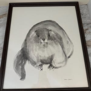 May include: A framed watercolor painting of a groundhog in shades of gray. The artwork features a fluffy, round groundhog with a small tail and tiny paws. The painting is signed in the bottom right corner and is set in a dark brown frame.