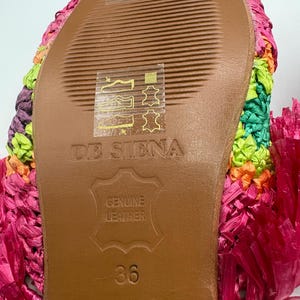 May include: Close-up of the sole of a colorful, woven sandal. The sole is brown leather with the text "DE SIENA" and "GENUINE LEATHER" embossed. The size is 36. The sandal is hand-embroidered in India.