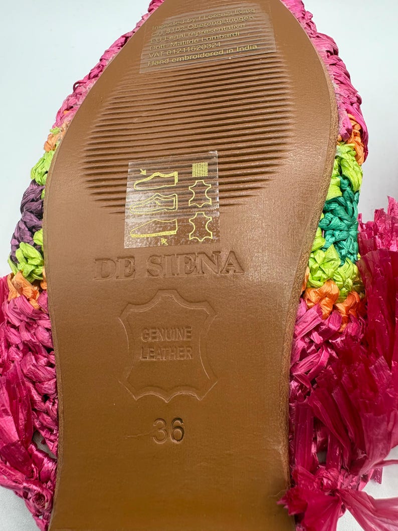 May include: Close-up of the sole of a colorful, woven sandal. The sole is brown leather with the text "DE SIENA" and "GENUINE LEATHER" embossed. The size is 36. The sandal is hand-embroidered in India.