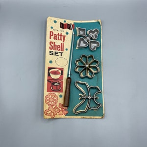 May include: Vintage set of aluminum patty shell molds with a wooden handle. The molds are shaped like a butterfly, flower, heart, and diamond. The package includes the text "ELPA Aluminum Patty Shell Set".