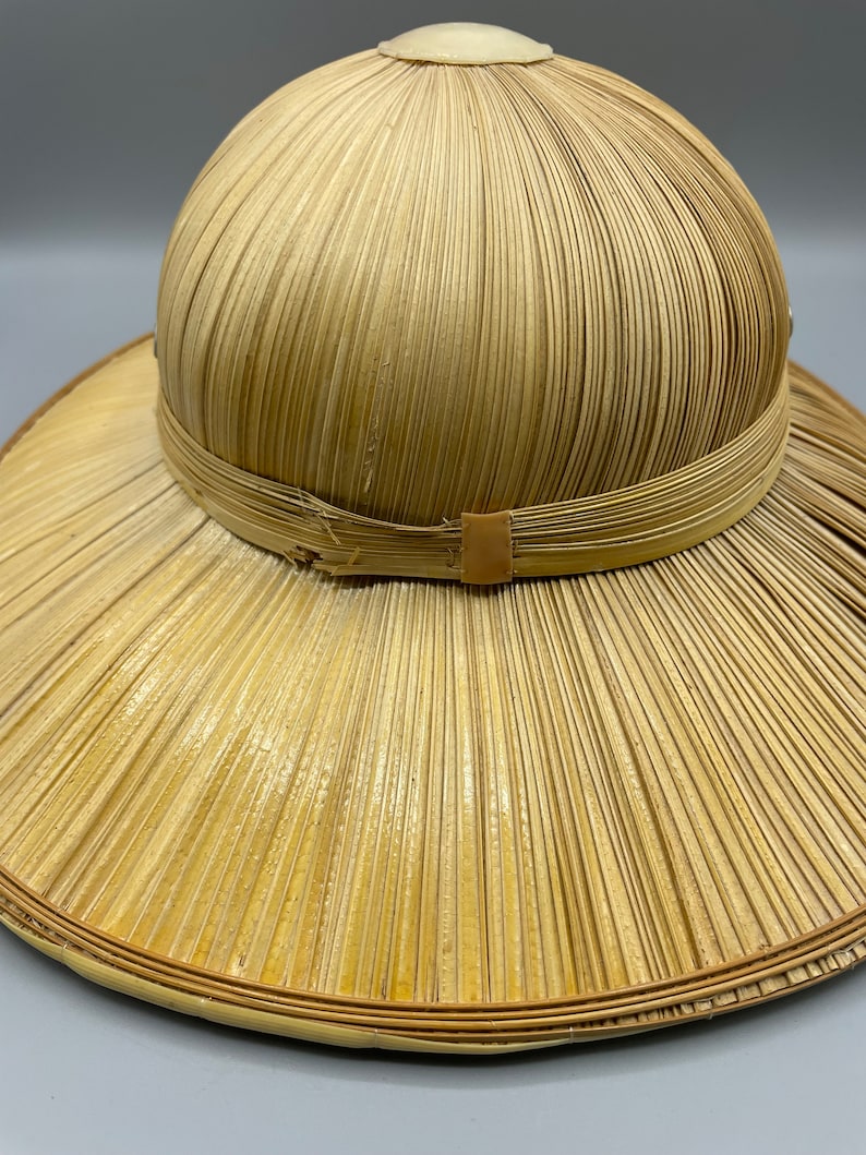 Puede incluir: Un sombrero de paja de ala ancha con una corona redonda. El sombrero est&aacute; hecho de paja tejida y tiene una banda de cuero marr&oacute;n alrededor de la corona.