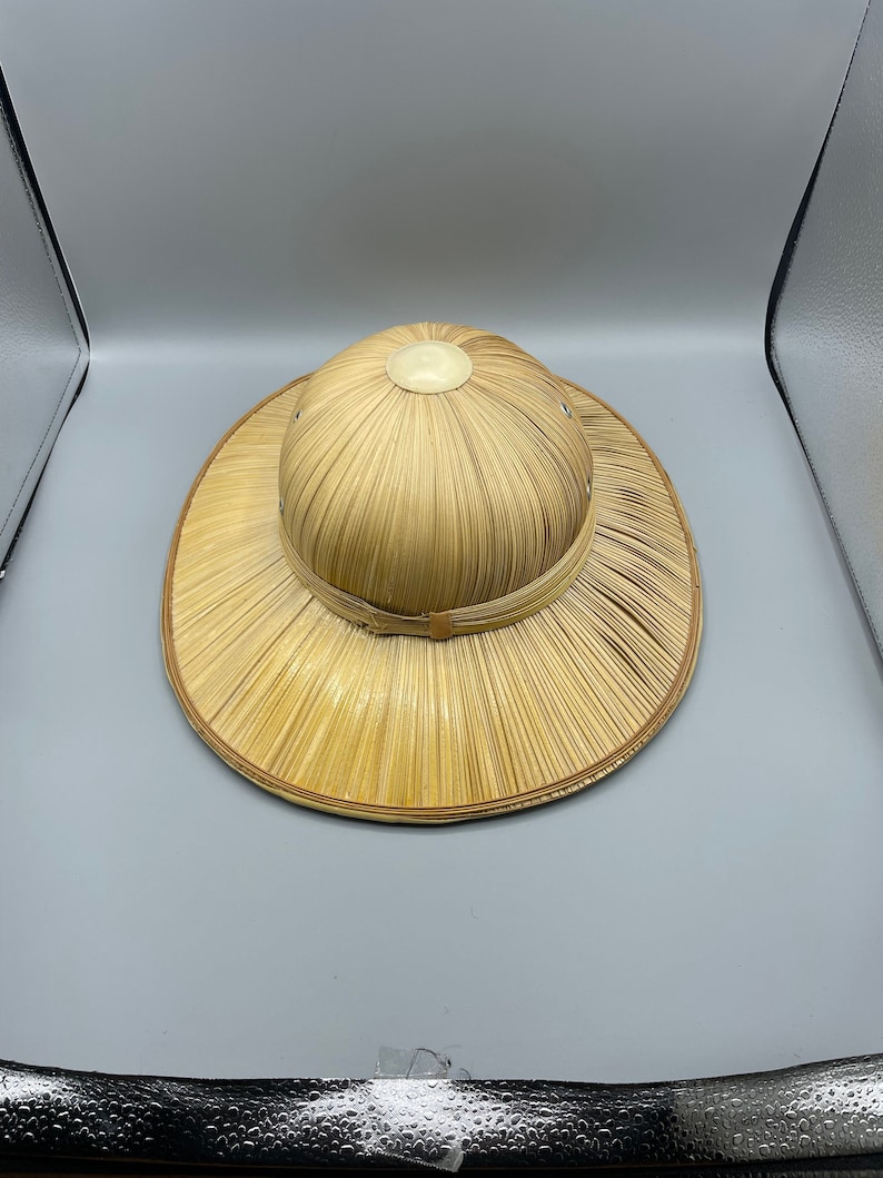 Puede incluir: Un sombrero de paja de ala ancha con una corona redonda. El sombrero est&aacute; hecho de paja tejida y tiene una cinta marr&oacute;n alrededor de la corona.