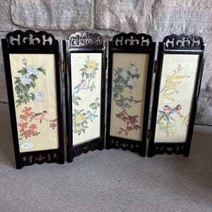 May include: A four-panel folding screen with black frames and decorative cut-out tops. Each panel features a different floral and bird illustration in shades of red, yellow, white, and blue on a cream background. The screen is made of wood.
