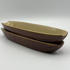May include: Two ceramic corn-shaped serving dishes. The dishes are stacked, with a textured, dark brown exterior and a tan interior. The elongated shape is ideal for serving corn on the cob or other side dishes.