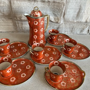 May include: A vintage tea set with a red and white floral pattern. The set includes a teapot, six cups, and six saucers.