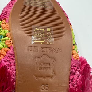 May include: Close-up of the sole of a colorful, hand-embroidered shoe. The sole is brown leather with the text "DE SIENA" and "GENUINE LEATHER" stamped on it. The shoe size is 36. The upper part of the shoe is a mix of pink, orange, and green.
