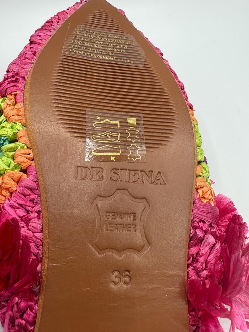 May include: Close-up of the sole of a colorful, hand-embroidered shoe. The sole is brown leather with the text "DE SIENA" and "GENUINE LEATHER" stamped on it. The shoe size is 36. The upper part of the shoe is a mix of pink, orange, and green.