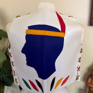 May include: White leather vest featuring a blue silhouette with a yellow headband and red feather. The vest has brown lacing on the sides and colorful accents at the bottom. The vest is displayed on a mannequin.