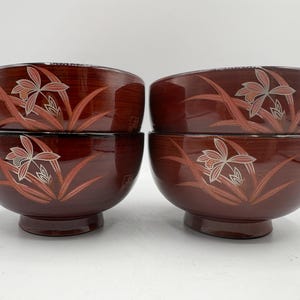 May include: Four wooden bowls with a dark reddish-brown finish. Each bowl features a floral design in shades of red and silver. The bowls have a rounded shape and sit on a short, pedestal base. The bowls are stacked in pairs.