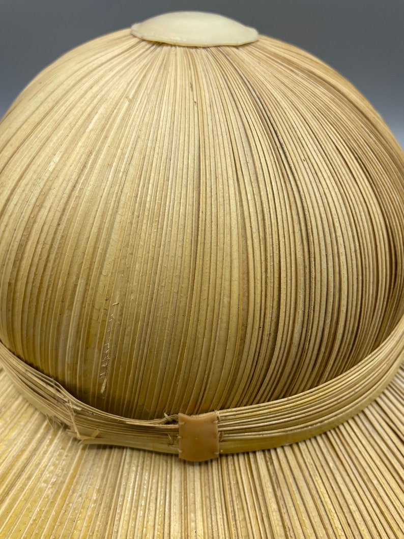 Puede incluir: Un sombrero de paja tejido con un ala ancha y una corona redonda. El sombrero est&aacute; hecho de paja natural y tiene una banda de cuero marr&oacute;n alrededor de la corona.