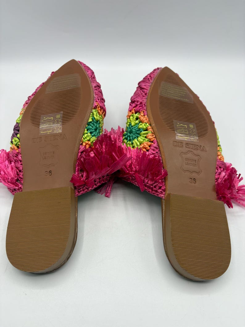 May include: A pair of colorful, woven mules. The soles are brown with the size 36 printed on them. The uppers are a mix of bright colors, including pink, green, orange, and purple. The heels have a pink fringe.