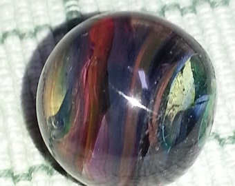 May include: A colorful glass marble with swirls of red, purple, blue, green, and gold. The marble is round and has a shiny, reflective surface.