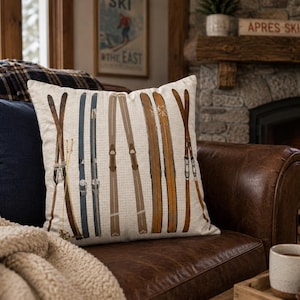 May include: A square throw pillow featuring a printed pattern of vintage-style wooden skis in shades of brown, tan, and blue arranged vertically against a light cream-colored background with a subtle grid texture across the entire fabric surface.