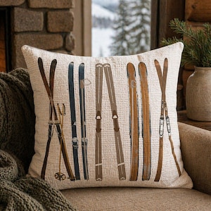 Puede incluir: Un cojín decorativo con un fondo crema que presenta un patrón de esquís vintage en varios tonos de marrón y azul. Los esquís están dispuestos verticalmente, creando un diseño rústico con temática invernal. El cojín está colocado sobre un sofá de tonos neutros.