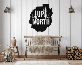 May include: Black metal wall decor with a silhouette of a forest and the text "Up North". The decor is hanging on a white wood wall above a wooden bench with a faux fur throw.