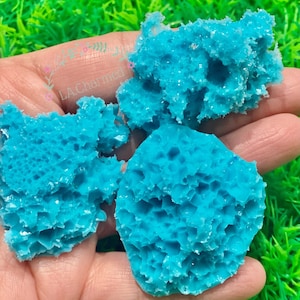 Puede incluir: Tres piezas de material azul brillante, poroso y con textura de panal de abeja con apariencia cristalina. Las piezas tienen bordes irregulares y dentados, y una estructura esponjosa con profundas hendiduras hexagonales en la superficie.