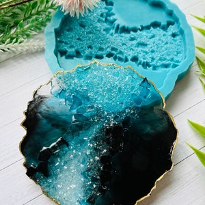 May include: A resin coaster with a gold edge, featuring a blend of black and turquoise hues. The coaster has a geode-like appearance with a textured surface. A matching turquoise silicone mold is in the background.