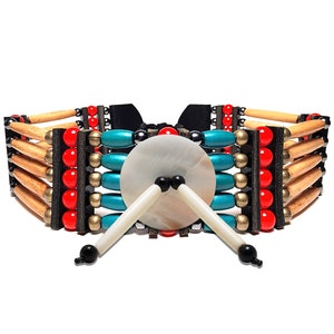 Puede incluir: Un collar gargantilla artesanal con un disco central de concha blanca y dos acentos blancos en forma de palillo. El collar incorpora clavijas de madera, cuentas rojas, turquesas y doradas, y detalles de cuero negro. El diseño es simétrico.