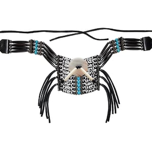 Puede incluir: Un collar artesanal con un panel central con estampado en blanco y negro, una concha grande y redonda de color claro y dos colmillos de color marfil. Tiene cuentas negras, detalles turquesa y cordones de cuero negro.