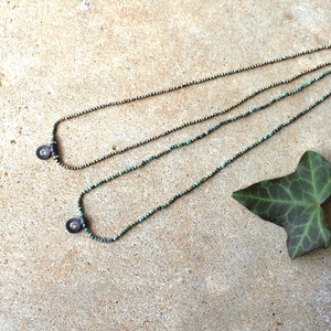 May include: Two delicate necklaces with small turquoise and silver beads and a silver charm at the end of each necklace.