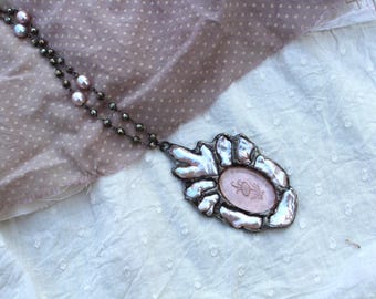 May include: A silver necklace with a pink cameo pendant featuring a floral design. The necklace is made of a chain with small silver beads and pink pearls.